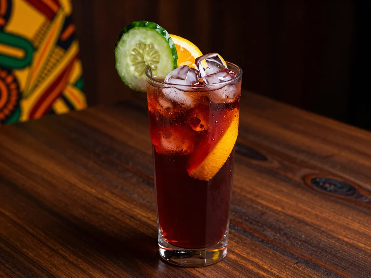 AI-generated photograph: A tall glass of red fruit punch with cucumber and orange slices